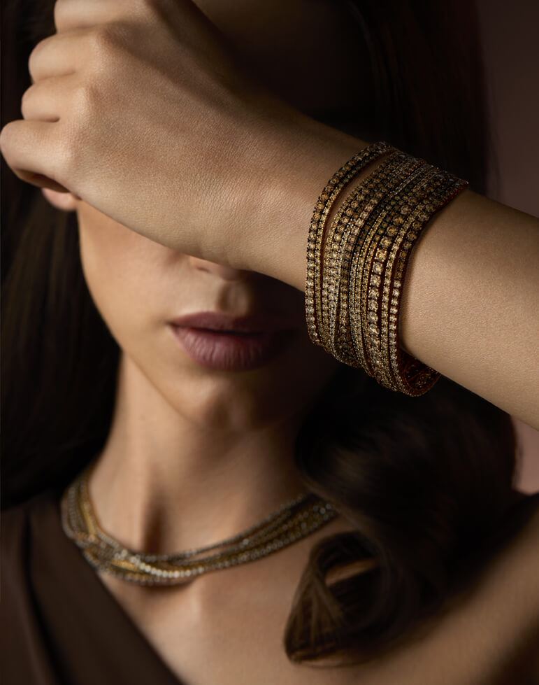 Elegant woman wearing Le Vian Chocolate Diamond® jewelry, featuring a multi-row chocolate and white diamond bracelet and matching necklace, with her arm raised across her face for a dramatic pose.