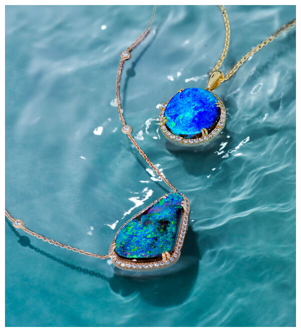 Two stunning Le Vian opal necklaces floating on rippling water, showcasing bold freeform blue and green opals set in yellow and rose gold with diamond halos.